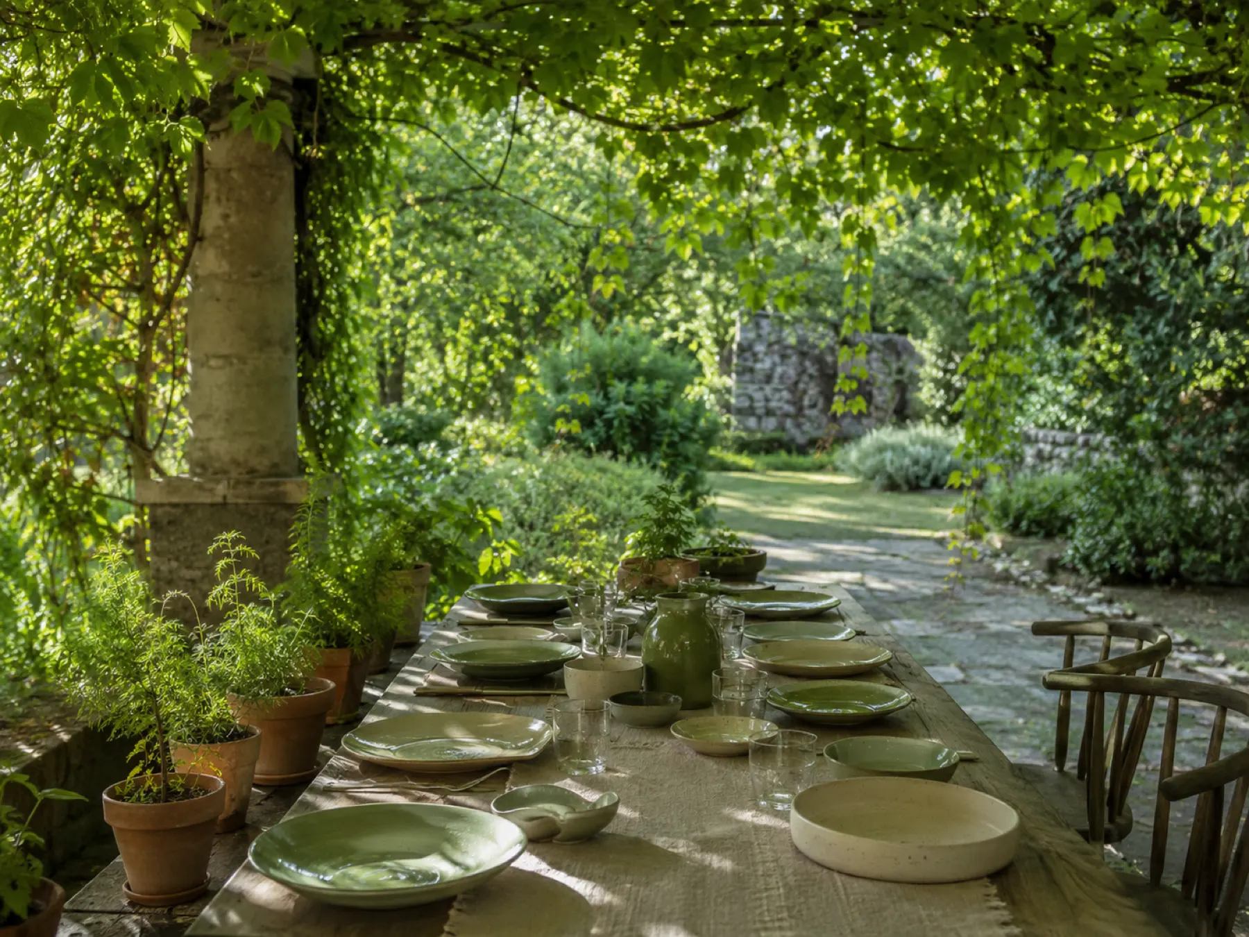 An intimate garden table with olive ceramics beneath a leafy pergola